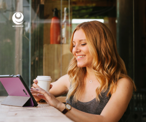Woman using tablet, smiling, holding coffee cup.