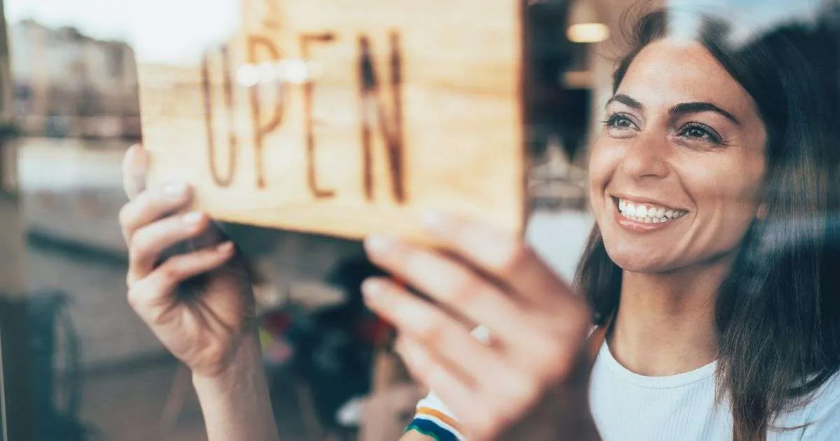 Smiling woman holding open sign in shop.