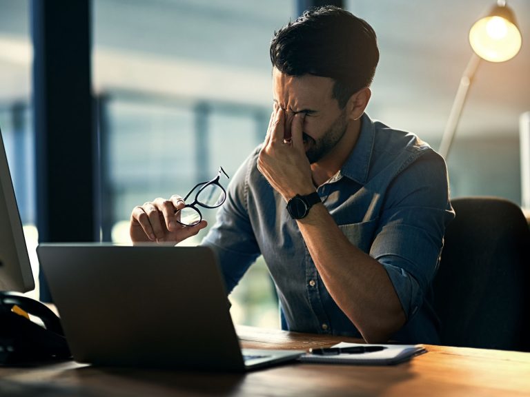 Stressed man holding glasses in front of laptop.
